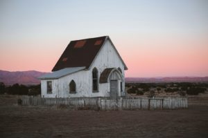 An abandoned, white church sits in the field.